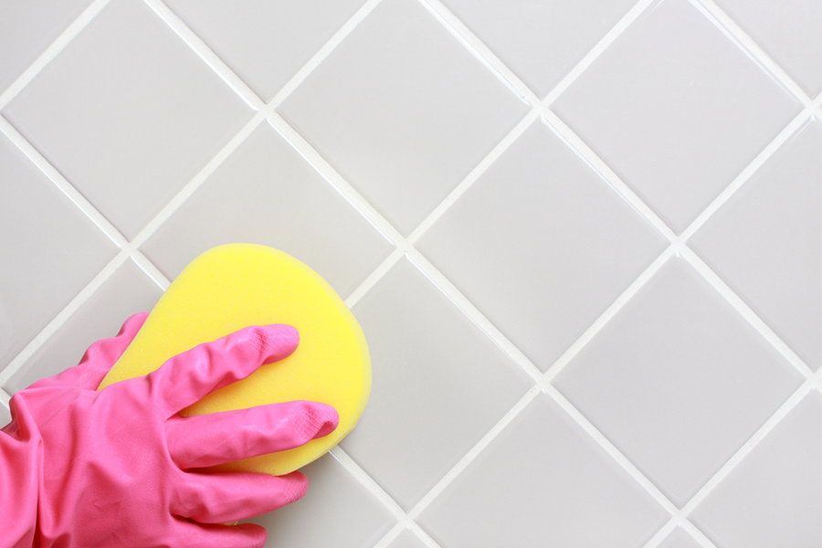 Pink gloves and white sponge cleaning grey tile and white grout.